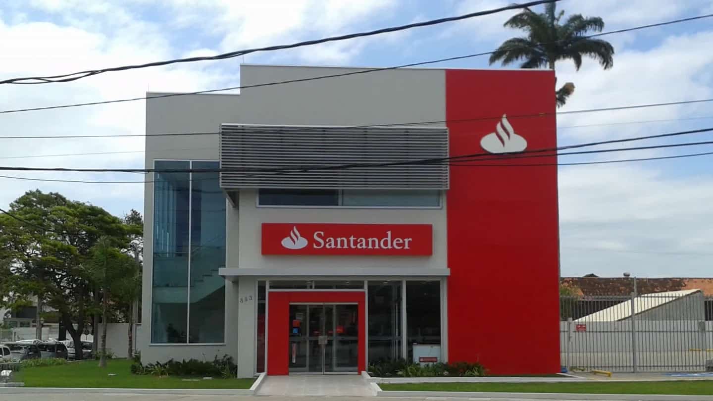Fachada de agência do Banco Santander no Brasil, com a placa da marca sobre a entrada de vidro.