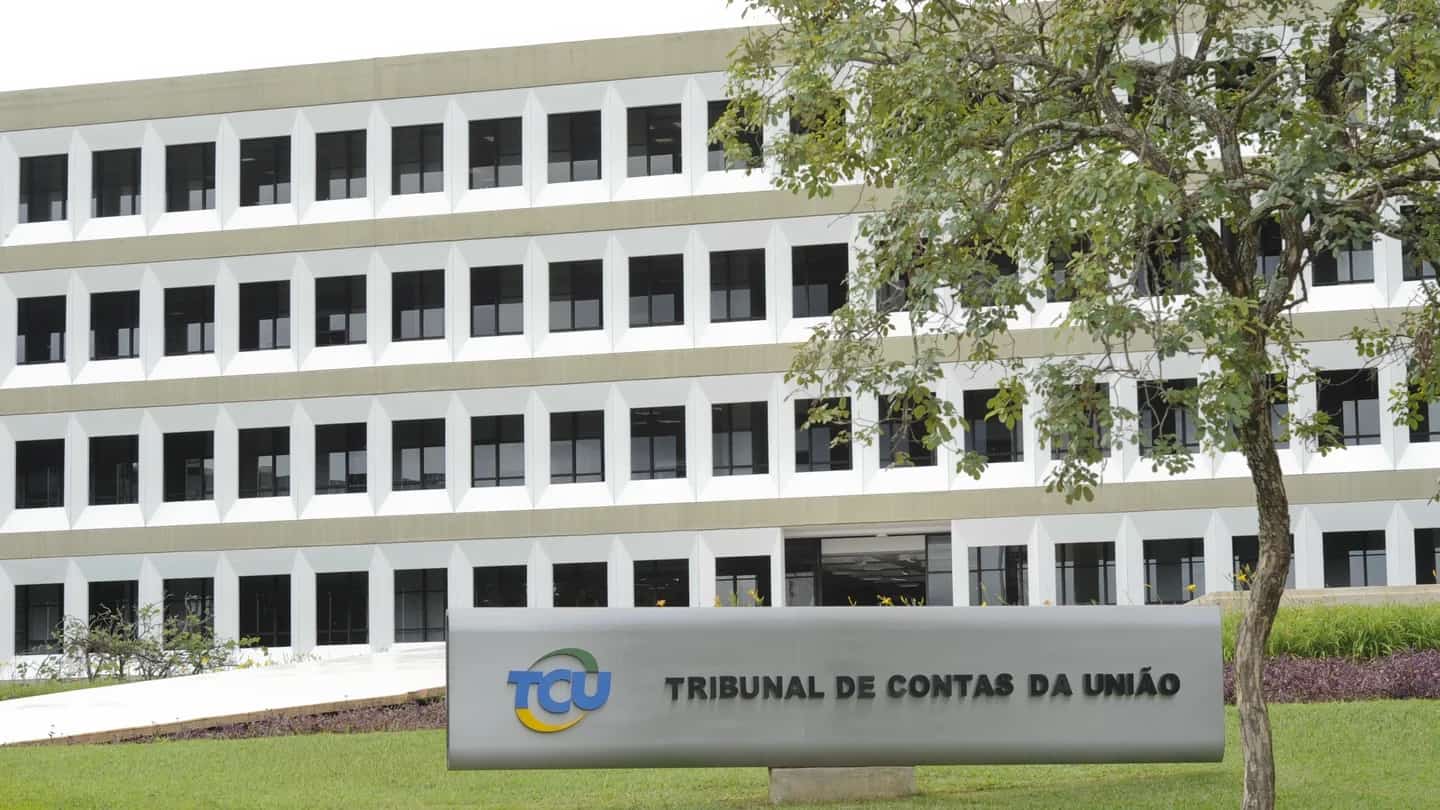 Placa de sinalização do Tribunal de Contas da União (TCU), em Brasília, com a fachada do edifício ao fundo.