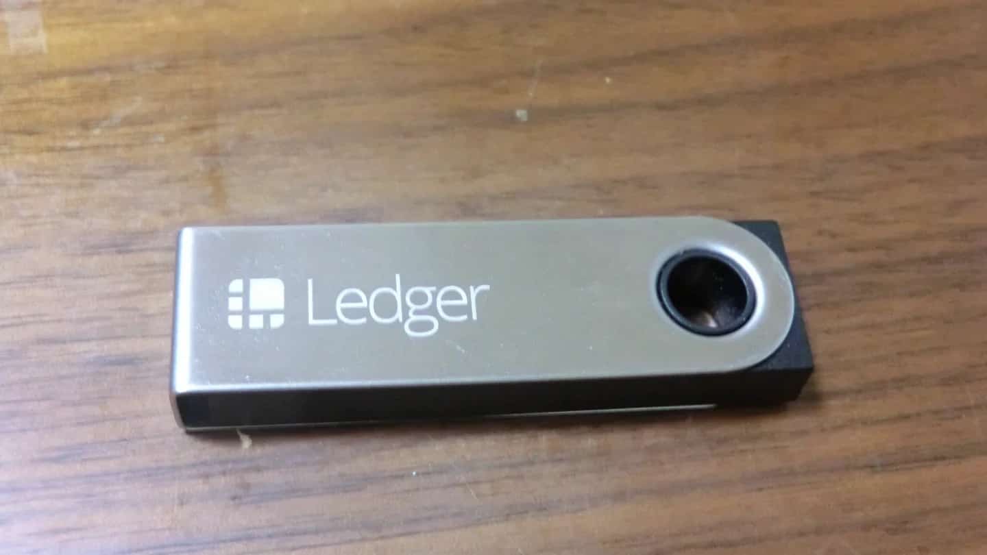 Dispositivo da Ledger, carteira física para guardar criptomoedas, sobre uma mesa de madeira.