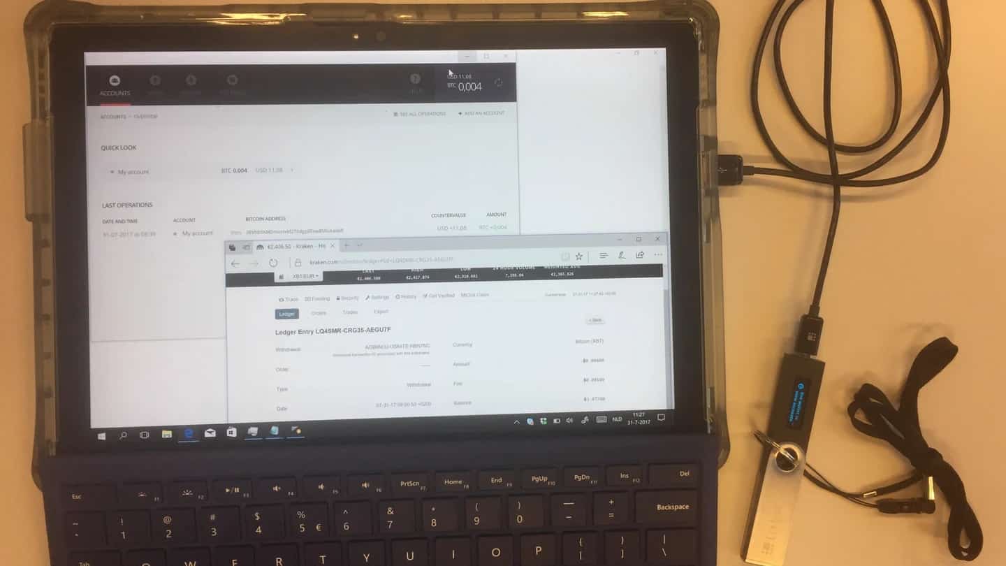 Tela de computador exibindo o painel de uma corretora de criptomoedas, com cabos e um dispositivo de hardware ao lado