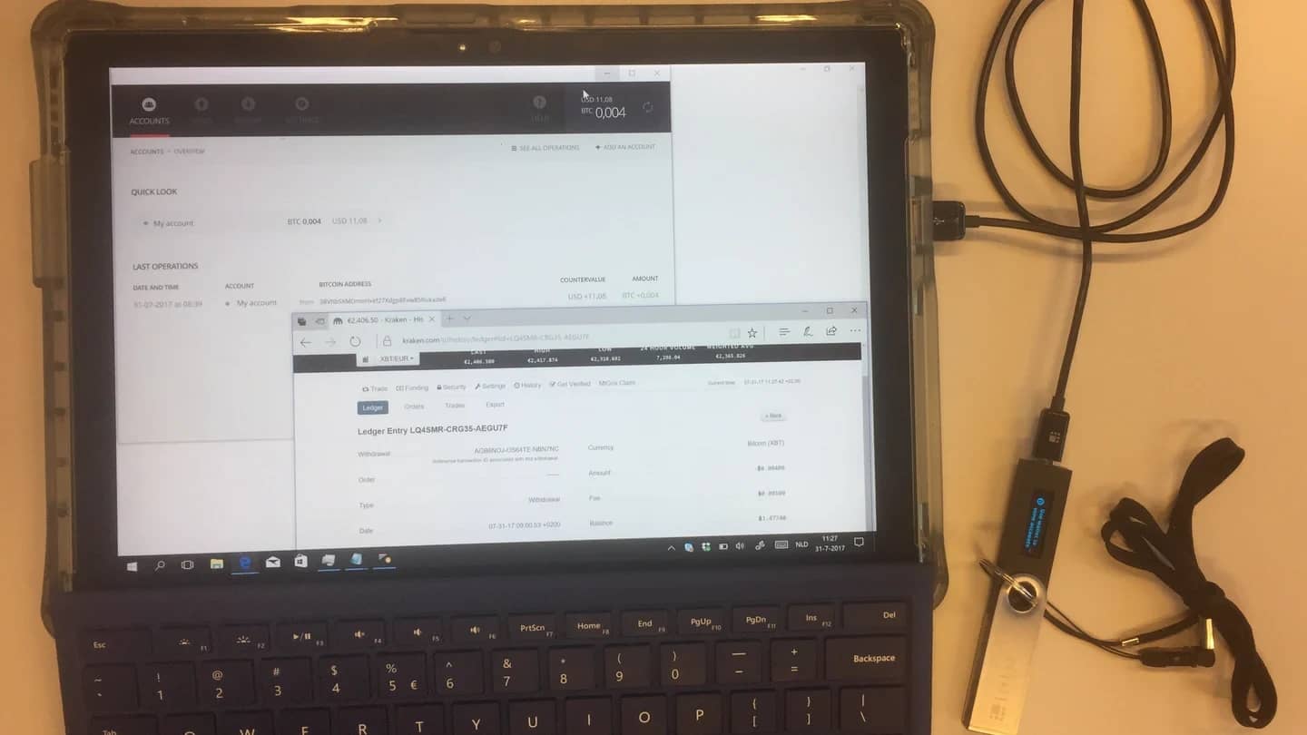 Tela de computador exibindo o painel de uma corretora de criptomoedas, com cabos e um dispositivo de hardware ao lado