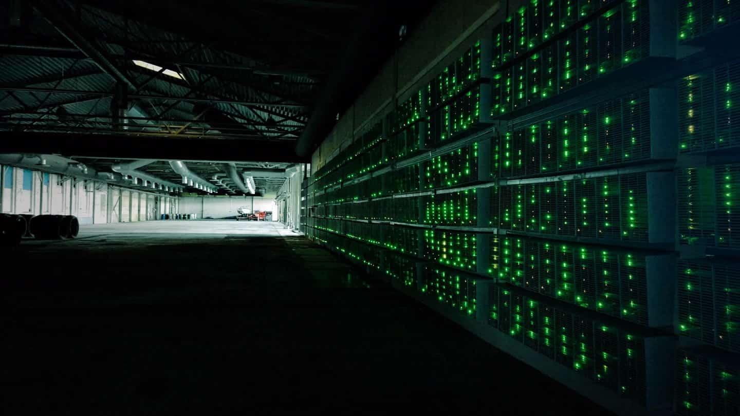 Interior escuro de fazenda de mineração de bitcoin com fileiras de equipamentos e luzes verdes