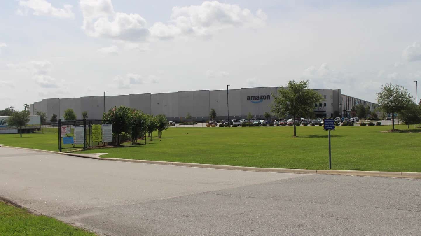 Galpão de centro de distribuição da Amazon com caminhões estacionados e estrutura metálica ao fundo