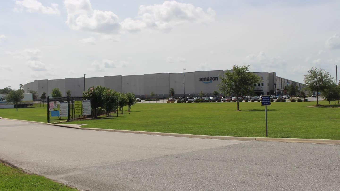 Galpão de centro de distribuição da Amazon com caminhões estacionados e estrutura metálica ao fundo