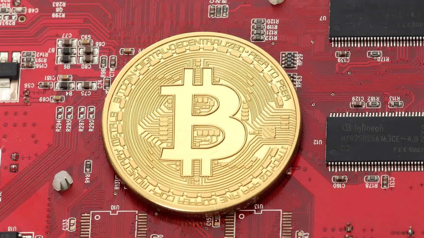 Moeda física de bitcoin banhada a ouro sobre placa de circuito impresso vermelha