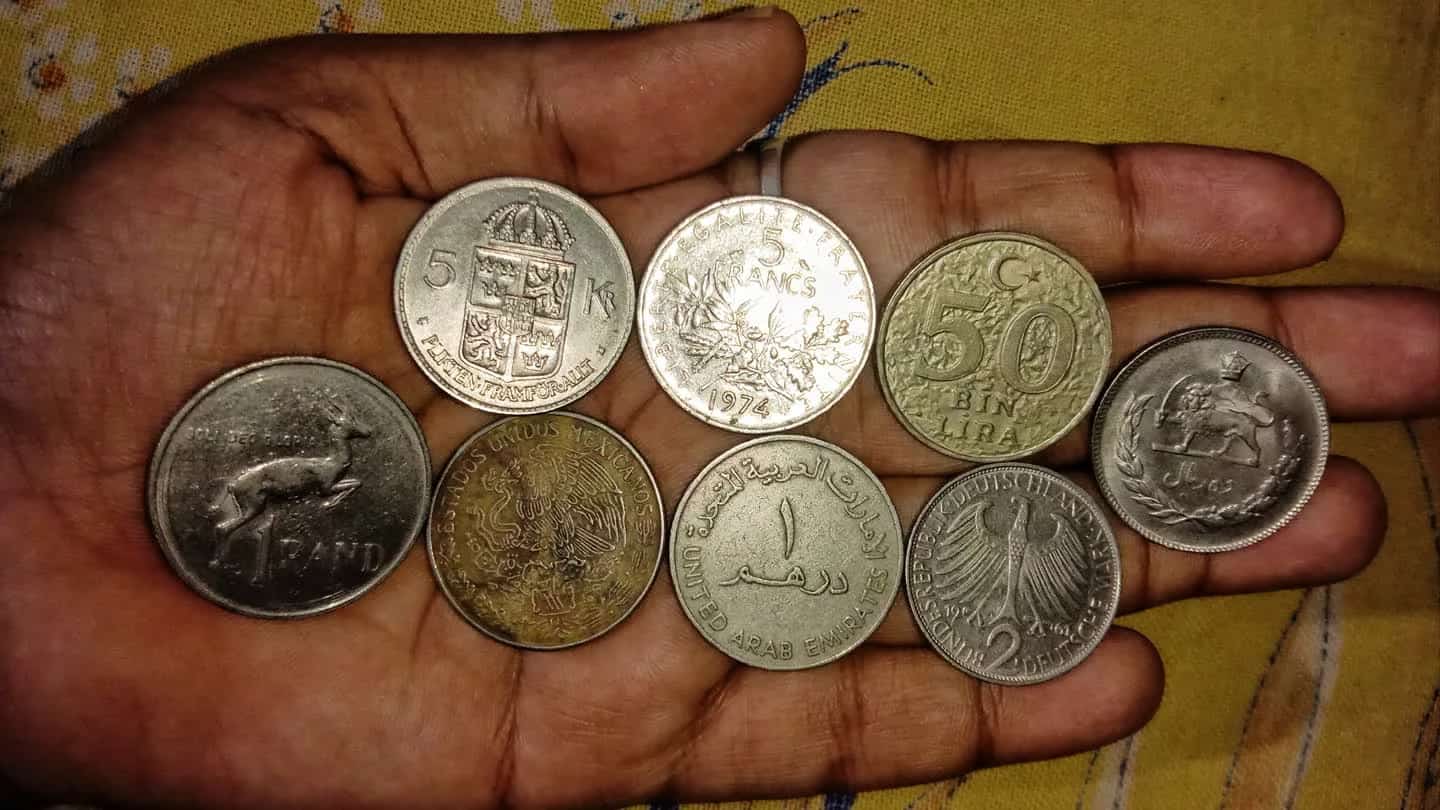 Mão segurando moedas de diferentes países, representando a diversificação de uma carteira