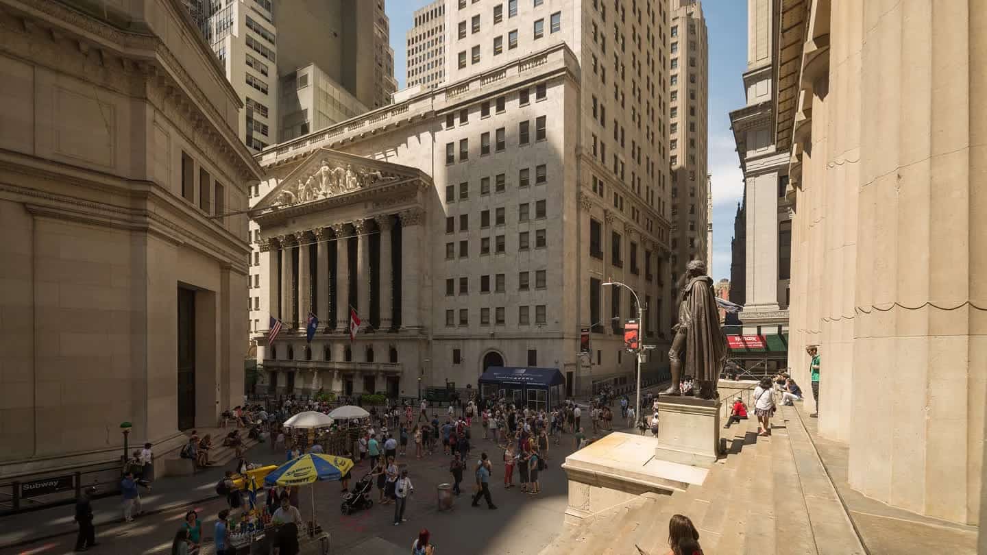 Fachada da Bolsa de Valores de Nova York, com colunas e movimento de pessoas na rua