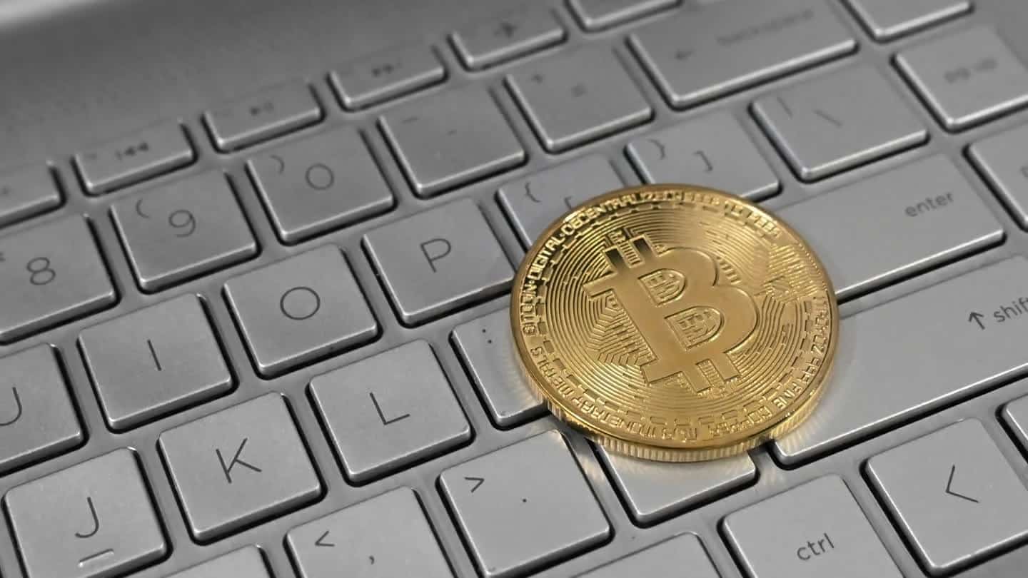 Moeda física de bitcoin apoiada sobre o teclado de um laptop