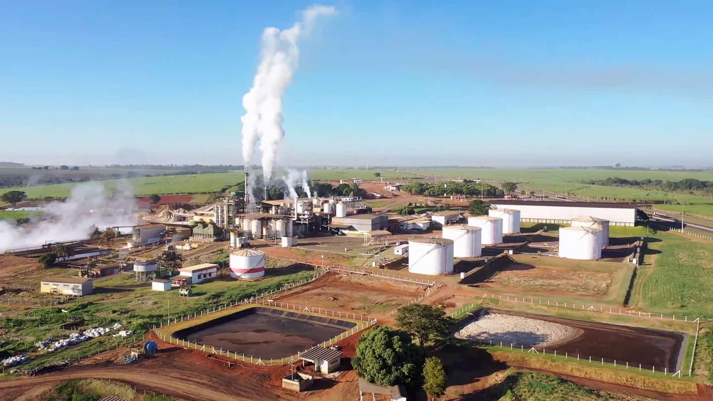 Vista aérea de usina de açúcar e etanol da Raízen, com silos e canavial ao fundo