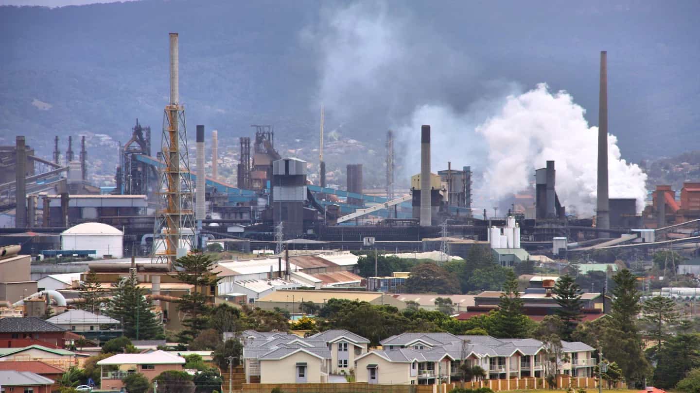 Vista aérea de usina siderúrgica com altos-fornos, chaminés e emissão de vapor.